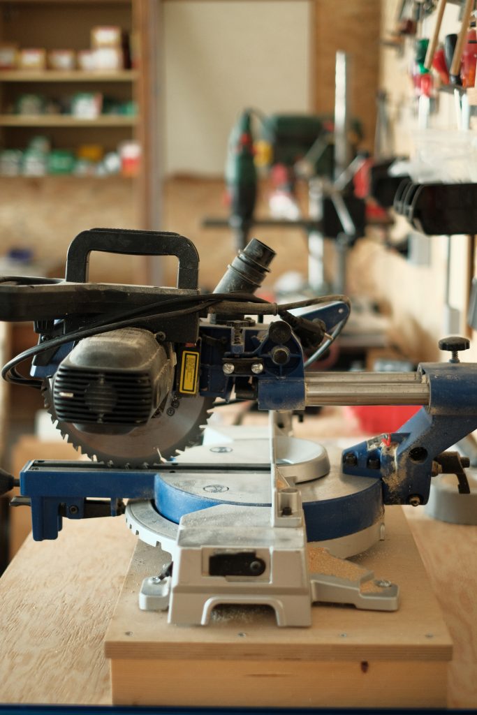 Detailfoto aus der Holzwerkstatt, das eine Kappsäge und im Hintergrund verschiedenes Werkzeug zeigt.